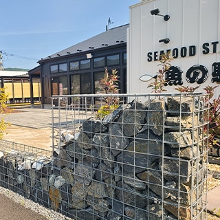 建物前に設置した段状のガビオン（蛇篭）。鉄線メッシュのボックスに灰色〜茶褐色の自然石を詰めた外構の景観例。